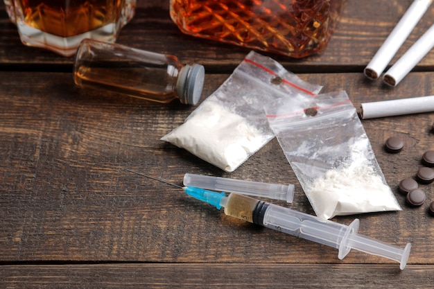 Verschillende verslavende drugs, waaronder alcohol, sigaretten en drugs op een bruine houten tafel. Drugsverslaving concept