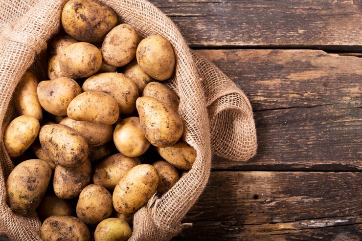 Foto verse aardappelen in zak op houten tafel, bovenaanzicht