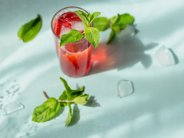 Verse aardbeicocktail. zomer roze cocktail met aardbei en ijsblokjes op lichtblauw