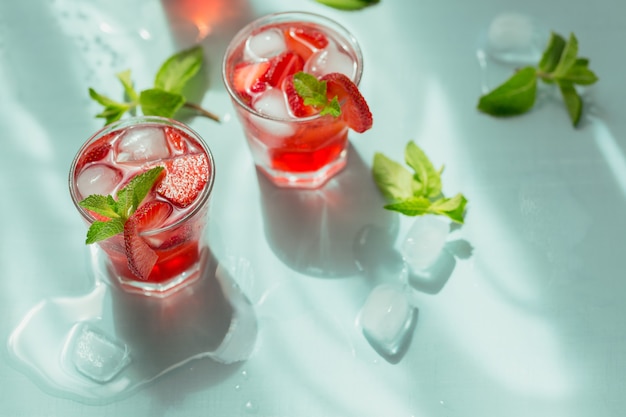 Verse aardbeicocktail. Zomer roze cocktail met aardbei, groene muntblaadjes en ijsblokjes op lichtblauw