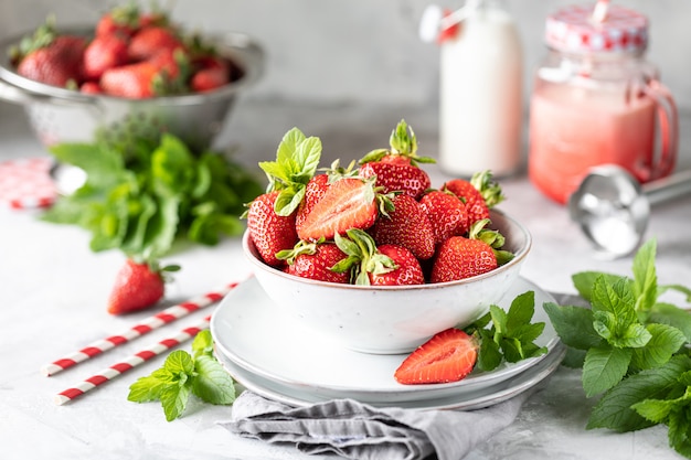 Verse aardbeien in een kom en takjes munt op een witte betonnen tafel. Ingrediënt voor smoothies.