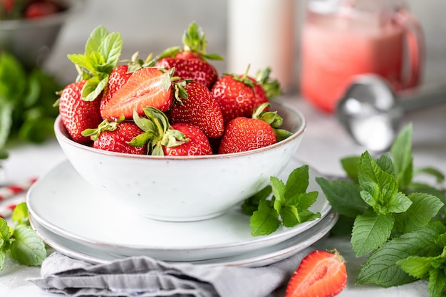 Verse aardbeien in een kom en takjes munt op een witte betonnen tafel. Ingrediënt voor smoothies.