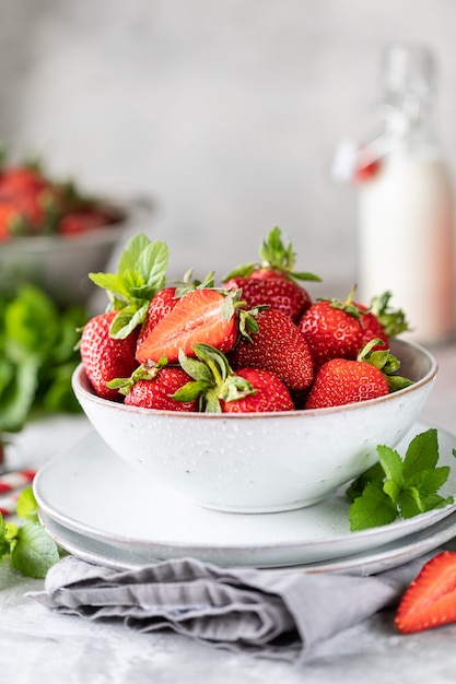 Verse aardbeien in een kom en takjes munt op een witte betonnen tafel. Ingrediënt voor smoothies.