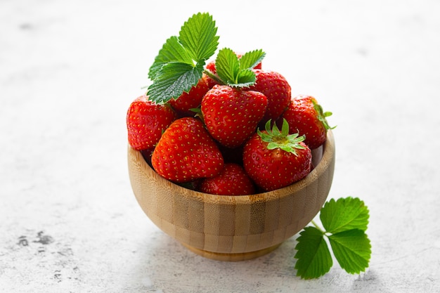 Verse aardbeien in houten kom met groene bladeren