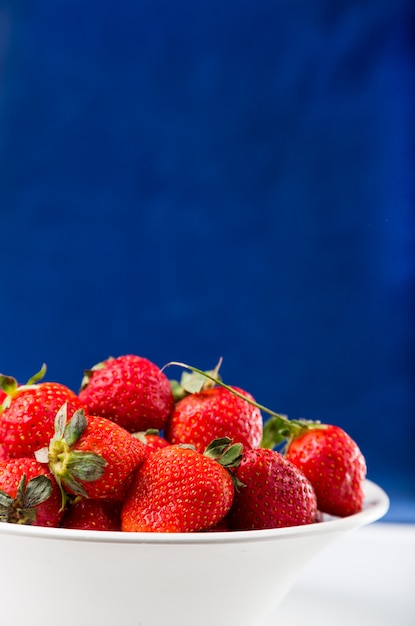 Verse aardbeien in witte plaat op blauwe achtergrond