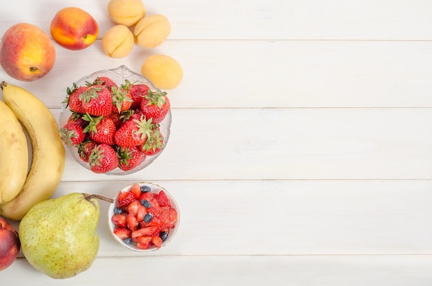 Verse aardbeien met fruit op een witte houten achtergrond met kopie ruimte. Ingrediënten voor fruitsalade.