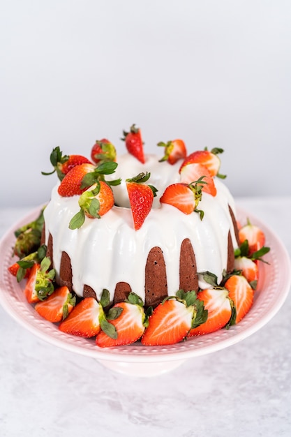 Verse aardbeien. Red velvet bundt cake met roomkaas frosting gegarneerd met verse aardbeien op een roze taart staan voor Valentijnsdag.