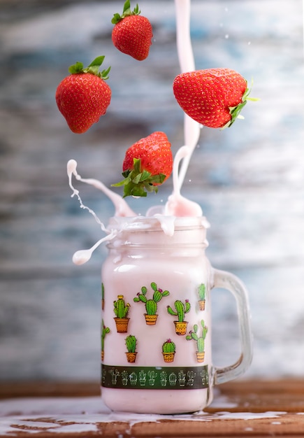 Verse aardbeien vallen in een glas om een heerlijke aardbei smoothie te maken. Houten muur