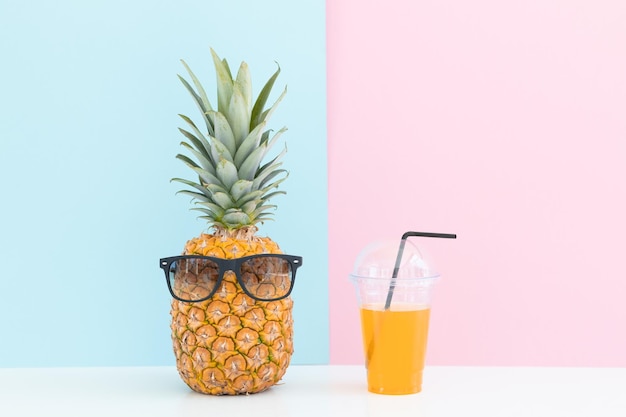 Verse ananas met zonnebril dichtbij een glas sap en een cocktailrietje op kleurenachtergrond