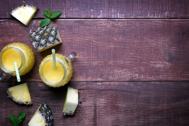 Verse ananasdrank met rietjes in twee glazen met fruit op een houten rustieke achtergrond