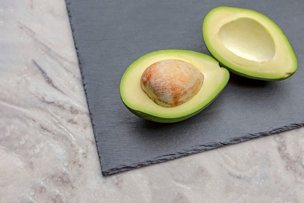 Verse avocado in tweeën gesneden. Een avocado met een bot ligt op een zwart stenen dienblad. Gezond voedselconcept.