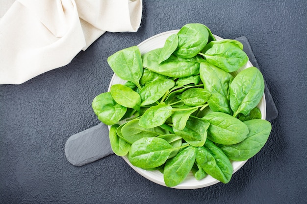 Verse baby spinazie bladeren in druppels water op een bord op een leisteen bord op een zwarte achtergrond. Vegetarisch, wellness en detox eten. Bovenaanzicht