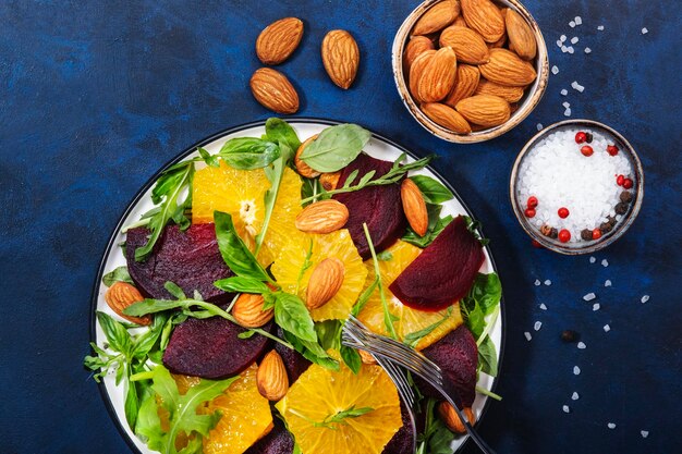 Verse bietensalade met sinaasappelrucola en amandelen op blauwe achtergrond Veganistisch gezond zomervoedsel Plat leggen Kopieerruimte