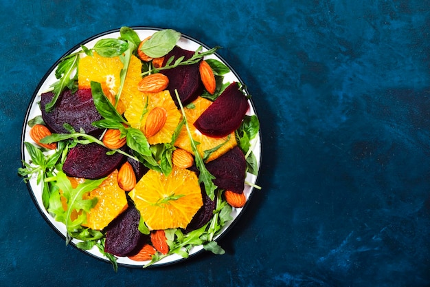 Verse bietensalade met sinaasappelrucola en amandelen op blauwe achtergrond Veganistisch gezond zomervoedsel Plat leggen Kopieerruimte