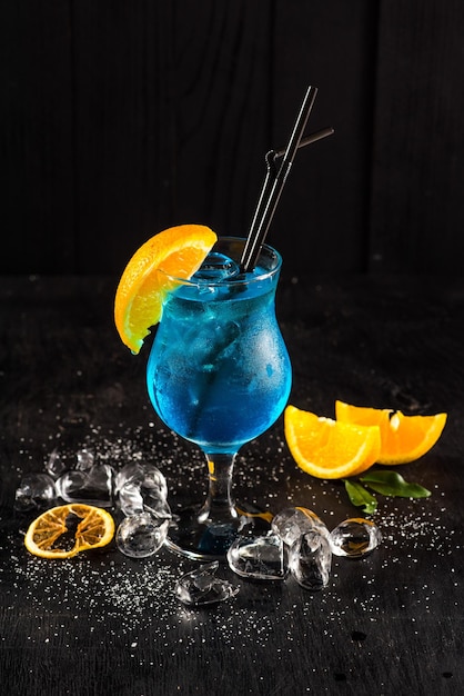 Verse blauwe cocktail met sinaasappel en ijs op zwarte achtergrond