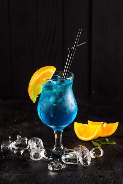 Verse blauwe cocktail met sinaasappel en ijs op zwarte achtergrond