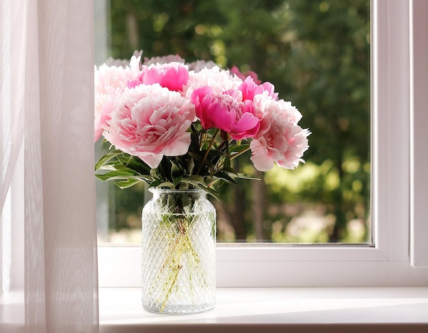 Verse bos roze pioenrozen in een glazen vaas op de vensterbank