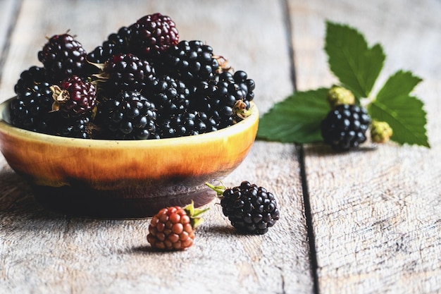 Verse bramen in een kom op houten tafel, rijp fruit en groene bladeren kopiëren ruimte