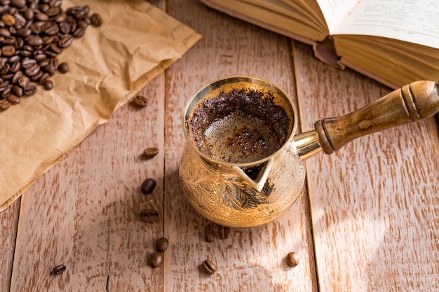 Verse breved koffie in cezve geopend boek en koffiebonen op houten lijst.