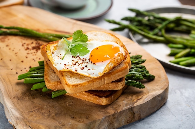 Verse broodjes met gebakken ei geserveerd met asperges, peper en peterselie op een houten snijplank