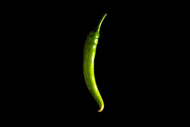 Verse chilipeper van groene kleur ligt op een zwarte achtergrond.