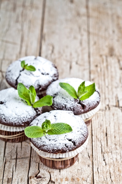 Verse chocolade donkere muffins met suikerpoeder en muntblad op rustieke houten tafel.