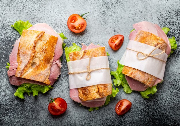 Verse ciabatta sandwiches met ham, kaas, sla, tomaten op stenen betonnen ondergrond, close-up, bovenaanzicht. Gezonde broodjes maken voor snack- of lunchconcept