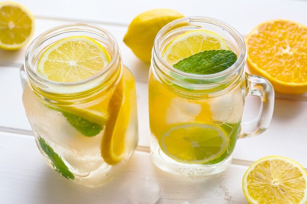 Verse citrus limonade met citroenen sinaasappelen munt en ijs op een witte houten tafel Zomer verfrissende drankjes