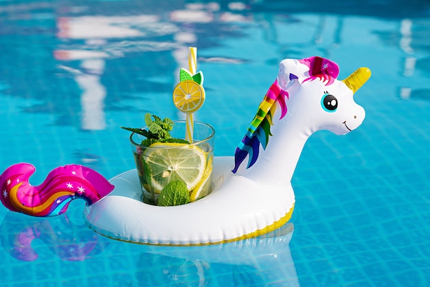 Verse coctailmojito op opblaasbaar wit eenhoornstuk speelgoed bij zwembad. Vakantie concept.