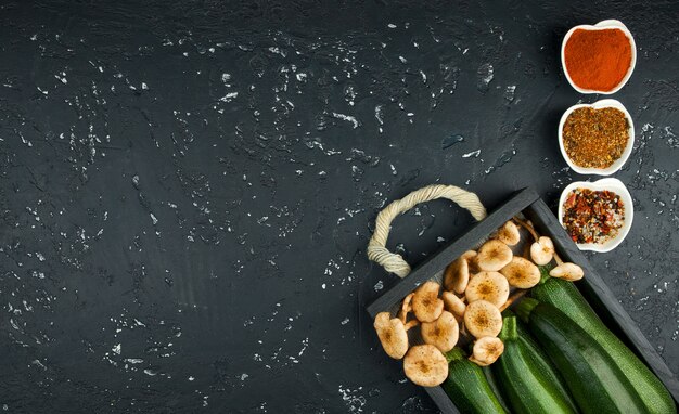 Verse courgette, champignons, kruiden en kruiden op een zwarte bord in bovenaanzicht met kopie ruimte