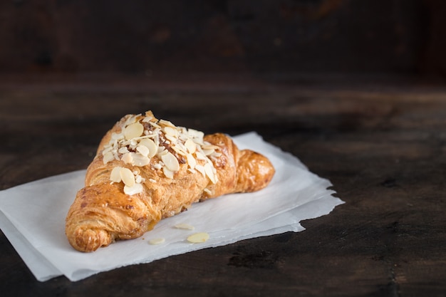 Verse croissant en koffie in een papieren kopje op donker