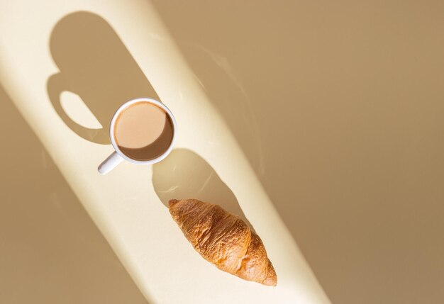 Verse croissant en kop warme koffie met melk in fel zonlicht Ontbijt op zomerochtend