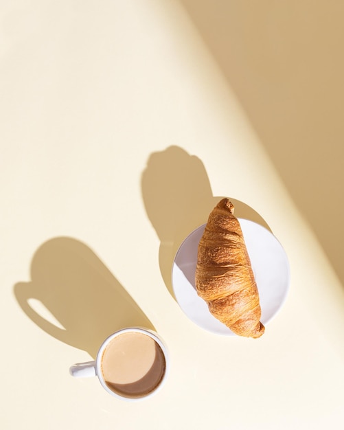 Verse croissant en kop warme koffie met melk in fel zonlicht Ontbijt op zomerochtend