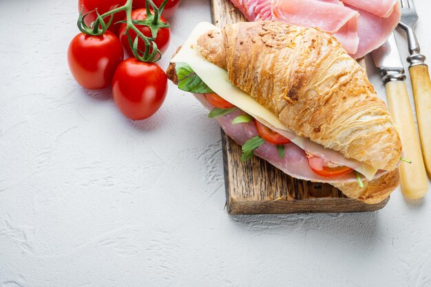 Verse croissant of sandwich met salade ham jamon prosciutto met kruiden en ingrediënten op witte stenen achtergrond met kopieerruimte voor tekst