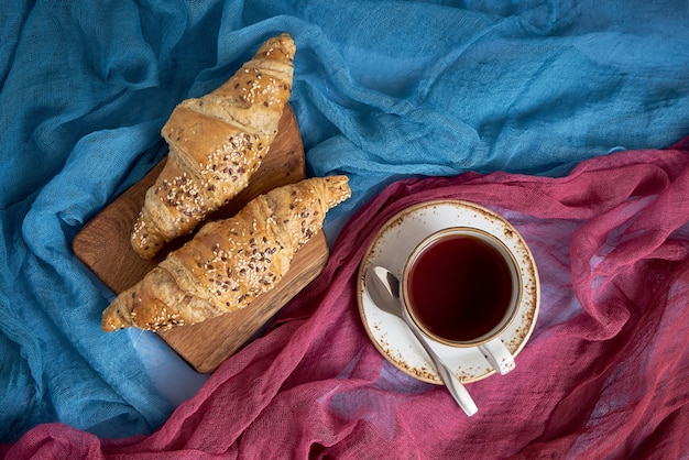 Verse croissants en kop zwarte thee op kleurrijke achtergrond.