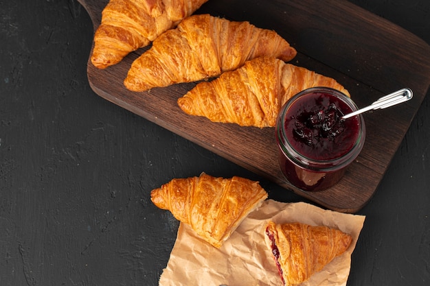 Verse croissants met bessenjam pot op zwarte houten bord