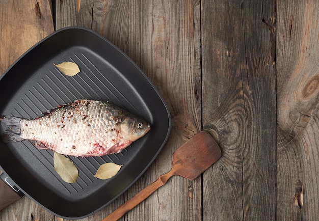 Verse crucian vis bestrooid met kruiden en ligt in een zwarte vierkante pan