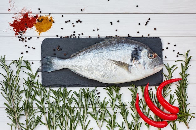 Verse dorado vis op leisteen snijplank met rozemarijn, kille peper op witte tafel. Bovenaanzicht, kopiëren