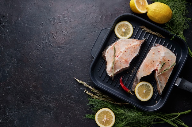 Verse filet van zeevis in een grillpan op donkere achtergrond.