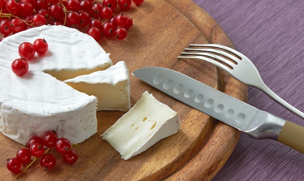 Verse Franse Brie-kaas onder witte schimmel op een houten bord met rode bes