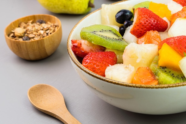 Verse fruitsalade in een kom Veelkleurig en tropisch fruit Ananas mango druif aardbei papaya meloen kiwi Extra met kastanjes en muesli Selectieve focus