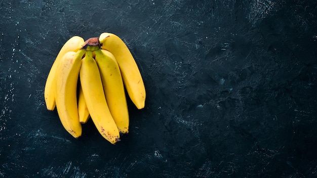 Verse gele bananen op een zwarte stenen tafel Bovenaanzicht Gratis kopieerruimte