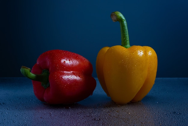 Verse gele en rode chilipepers blauwe achtergrond waterdruppels op glas