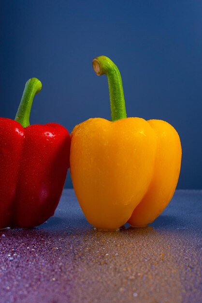 Verse gele en rode chilipepers blauwe achtergrond waterdruppels op glas.