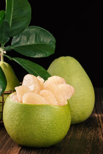 Verse gepelde pomelo grapefruit shaddock met groene bladeren op donkere houten plank tafel Seizoensfruit in de buurt van midautumn festival close-up kopieerruimte