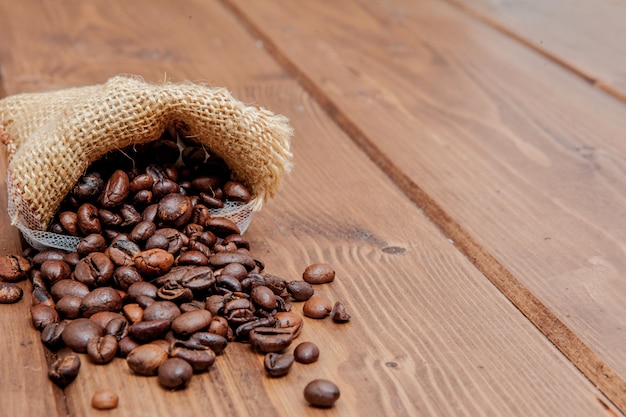 Verse geroosterde koffiebonen die de zak op de houten oppervlakte uitvallen.