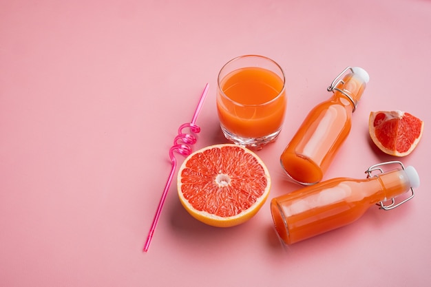 Verse grapefruits en glas grapefruitsap, op roze getextureerde zomerachtergrond, met kopieerruimte voor tekst