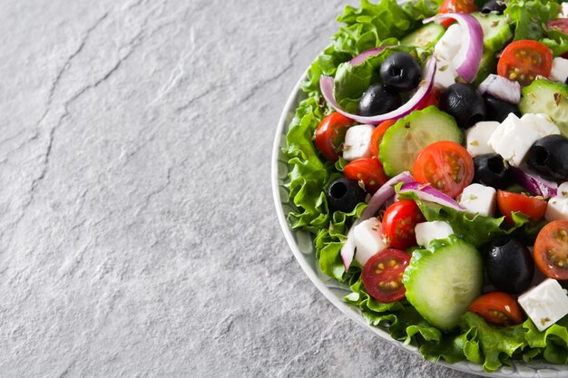 Verse Griekse salade in plaat met zwarte olijven, tomaat, feta-kaas, komkommer en ui op grijze achtergrond kopie ruimte