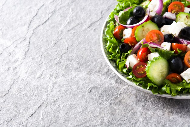 Verse Griekse salade in plaat met zwarte olijven, tomaat, feta-kaas, komkommer en ui op grijze Copyspace