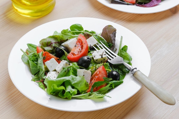 Verse Griekse salade in witte plaat op houten tafel achtergrond. Close-up bovenaanzicht.